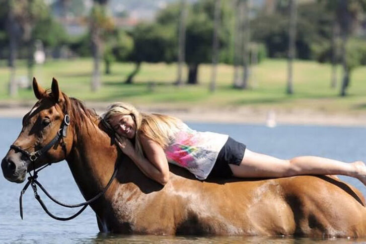 Debbie Steglic laying on the back of her horse in the water.